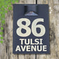 Modern acrylic house number sign with integrated solar light mounted beside a front door, glowing softly at night.