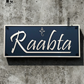 Gold and matte black acrylic Ganesha house number sign mounted beside a modern front door exterior wall.