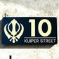 Kandha house number plaque in black acrylic with metallic gold lettering mounted on exterior wall.