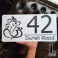 Front view of a matte black and white Ganesha house number sign mounted on exterior wall.