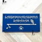 Navy blue house number sign featuring a flute design and evil eye detail mounted on a wall.