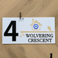 White flute house number sign mounted on exterior wall with decorative evil eye.