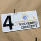 Modern white house number sign with evil eye accent beside home entrance.